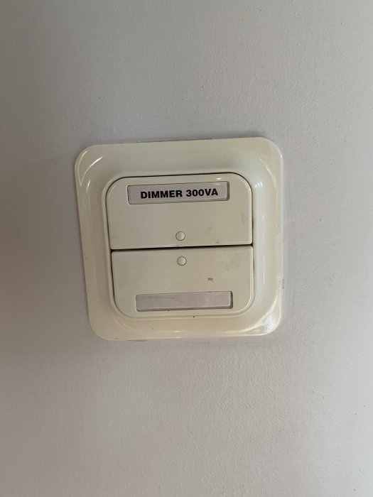 Dimmerknapp på vägg märkt 'DIMMER 300VA', beigefärgad, med på/av knapp och dimningsfunktion.
