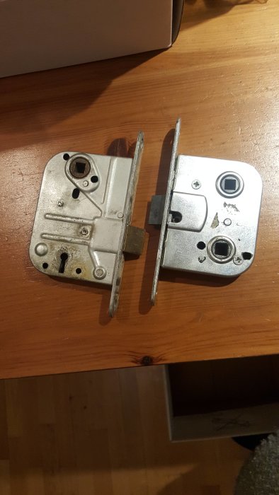 Två låshus bredvid varandra på ett träbord, det ena ser äldre ut med tydligare slitage och smalare design.