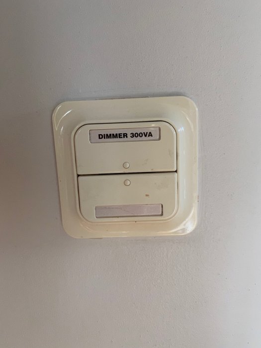 Äldre dimmerströmbrytare på vägg, märkt "DIMMER 300VA", med tecken på användning.