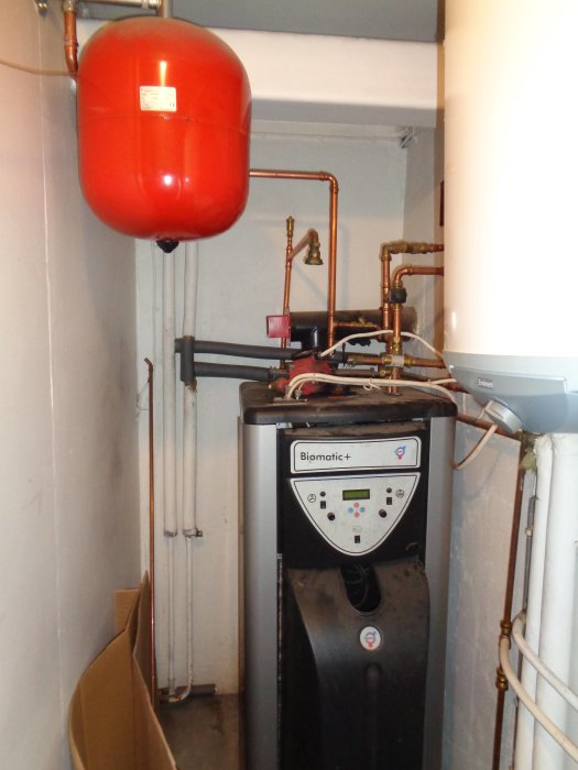 Värmesystem med panna och röda rör, plus påsar med pellets till höger, till salu för 5500 SEK.