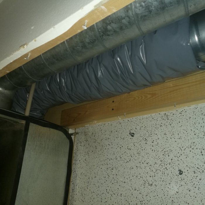Installation av ljuddämpande material runt ventilation inomhus, synlig t-skarv och isolerade rör.