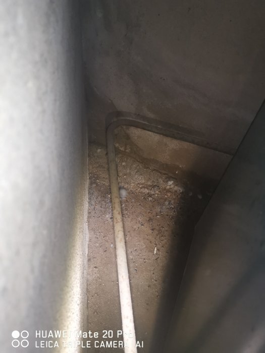 Hörn av ett garage med tecken på fuktläckage vid kabelgenomföringen och på betongytan.
