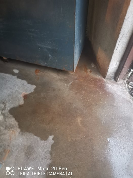 Vattenläckage på garagegolvet med tydliga fläckar och en del av en blå dörr.