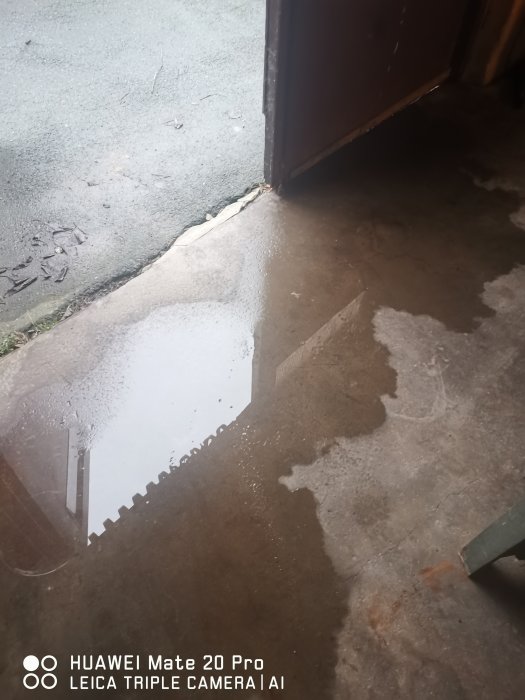 Vattenpöl på garagegolv med spegling av dörren tyder på läckage.