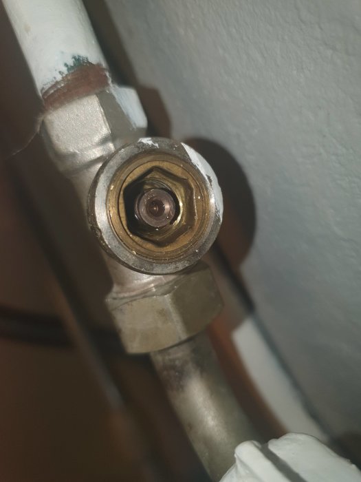 Närbild av en radiatorkoppling med en centralt placerad plupp som användaren testar att vrida för att minska sprutning.