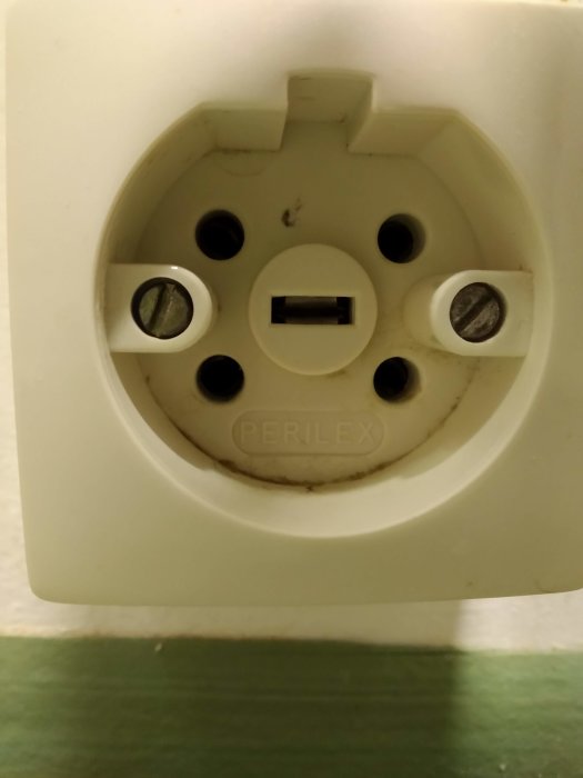 En vit Perilex-väggkontakt med plats för fyra stift, men med endast tre stift synliga.