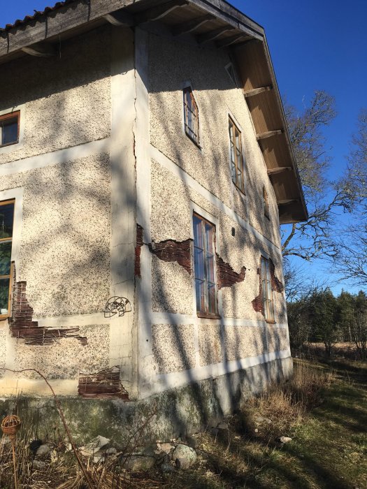 Slitet hus med spruckna och flagande ytterväggar och skadad puts som behöver renovering.