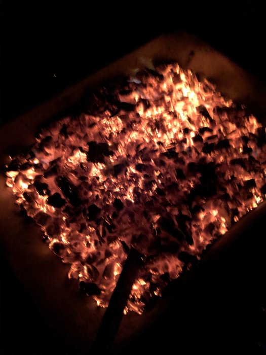 Glowing embers in a burn pile at night with a shovel.