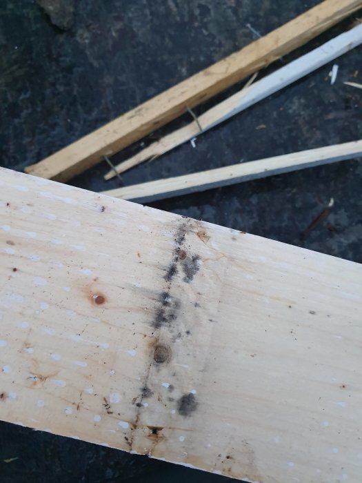 Nyligen borttagen träpanel med tecken på svart mögel eller påväxt där läkten har varit fästad, mot bakgrund av mer demonterat trä.