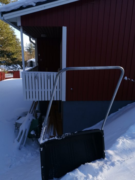 En snösläde vält framför en röd trästuga med snö runtomkring.