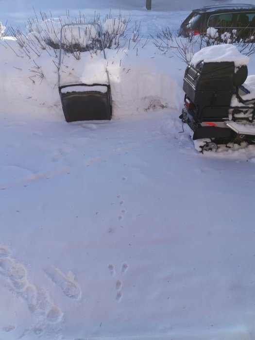 Snöig uppfart med begravd bil och snöskyffel, fotspår i snön.