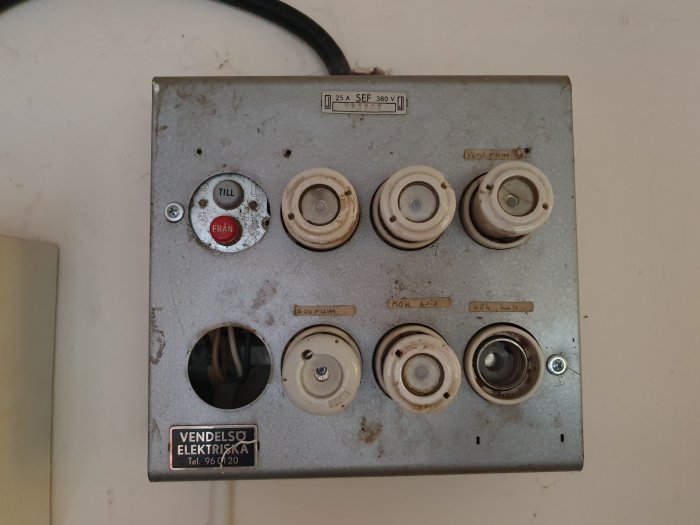 Gammal säkringsbox med etiketterade säkringar för vardagsrum, kök och hall.