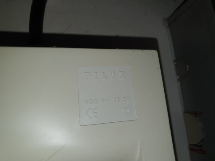 Närbild på en RILUX-märkning på en vit elinstallationsbox, 400 V - IP30 indikerat, i ett garage.