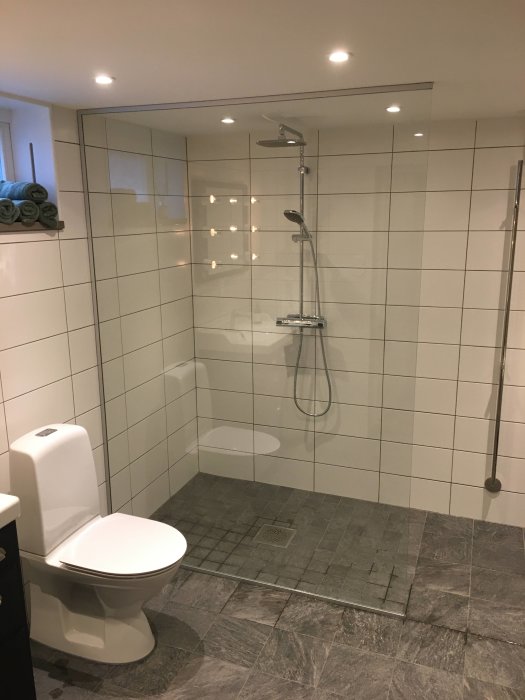 Nyrenoverat badrum med duschkabin, toalett och vita kakelväggar.