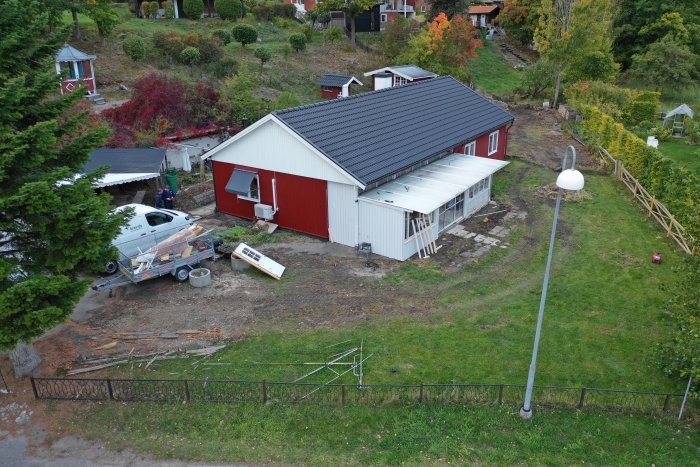 Röd vit husbyggnad under renovering, saknar altan, byggmaterial synligt, trädgård.