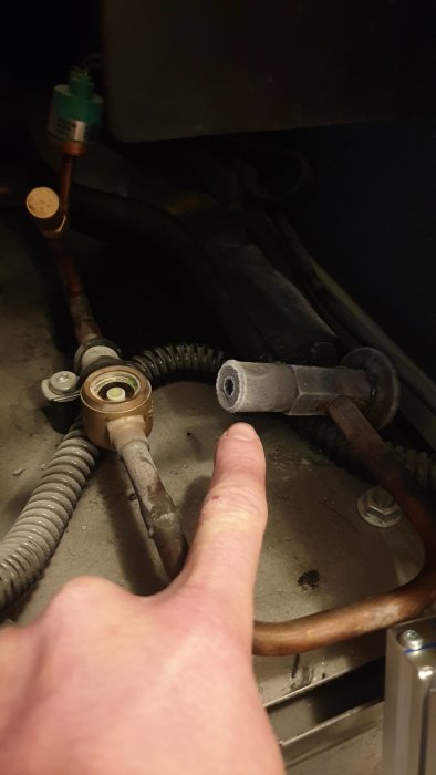 Hand pekar på frosttäckta rör nära en trycksatt ventil, antyder kyla i en kompressoranläggning.