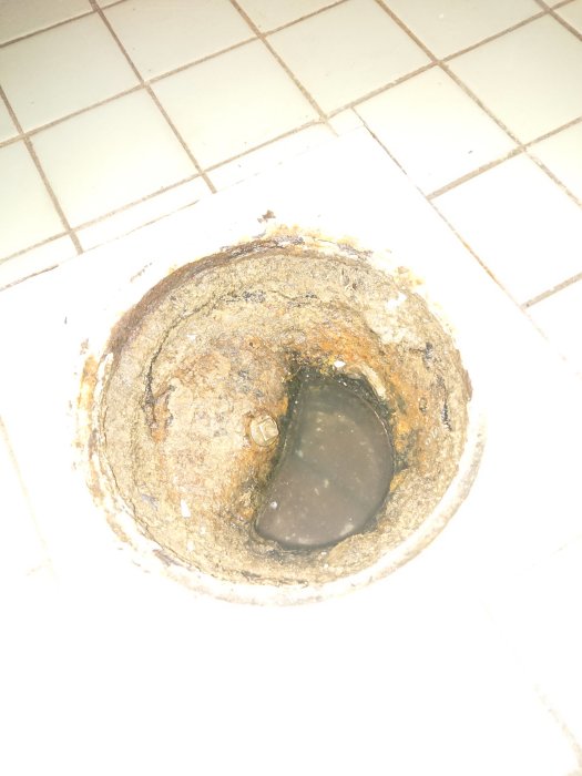 Igengrodd rensbrunn i badrum med synlig rensplugg och missbildad skruvfyrkant, behöver reparation.