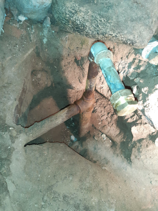 Vattenledningsrör i mark med T-koppling och rost som går vertikalt uppåt och horisontellt.