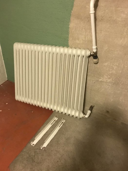 Vit radiator 95x75 cm med termostat och avtagbara fästen mot en vägg.
