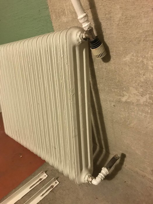 Vit radiator med termostat och fästen monterad på vägg, längd 95 cm och höjd 75 cm.