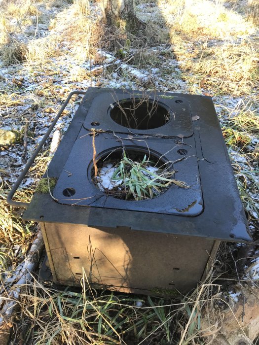 Gammal vedspis övergiven i skog med snöfläckar och frost på gräset.