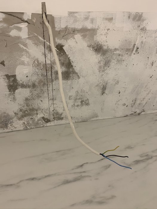 Elektrisk kabel med exponerade ledare mot en vägg och marmorbänkskiva, föreslagen för anslutning till diskmaskin.