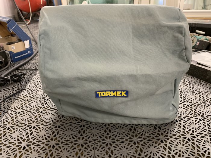 Tormek T-8 slipmaskin täckt med skyddsöverdrag och Tormek-logotyp, placerad på ett mönstrat bord.