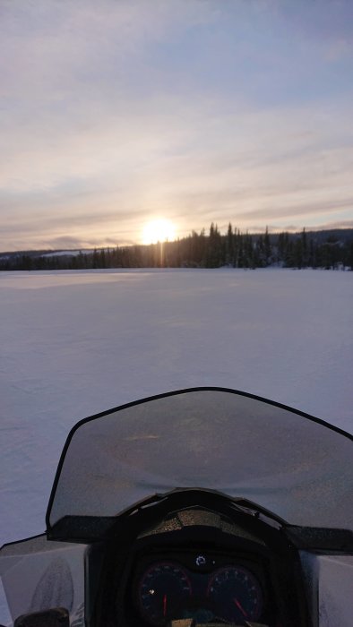 Vy över snölandskap från snöskoter med solnedgång i bakgrunden.