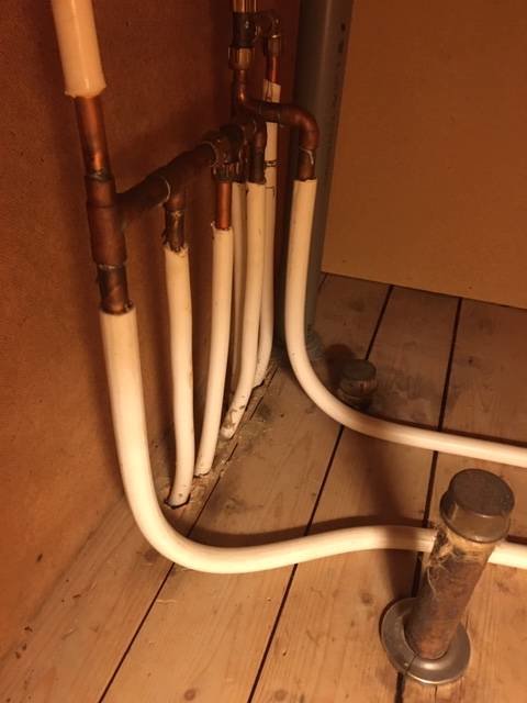 Plaströr och kopparledningar i ett kryputrymme som indikerar vattenledningar för varmt och kallt vatten.