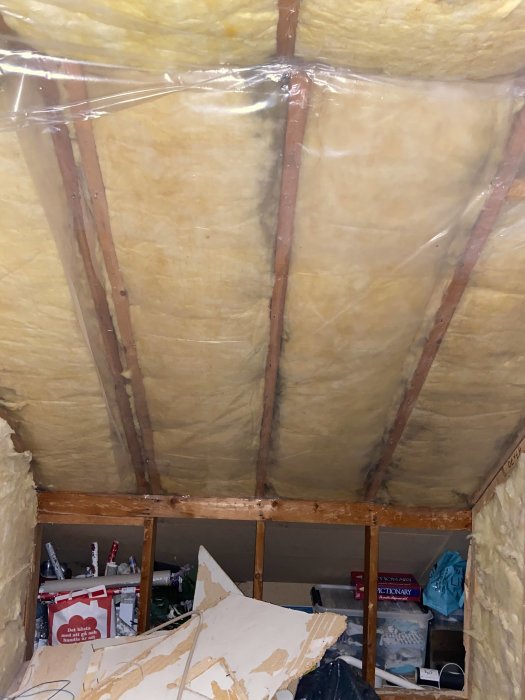 Delvis rivet badrumstak med isolering och träreglar, möjlig takstol och byggavfall.
