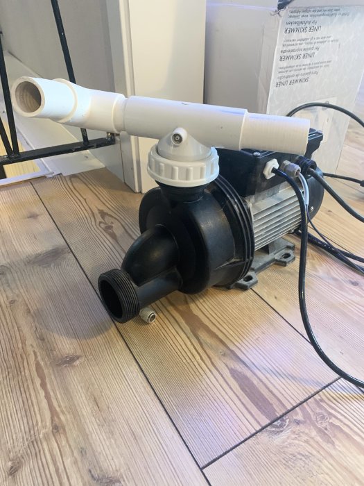 Jetpump och vita PVC-rör på trägolv, tänkt för bräddavlopp och bubbelinstallation.