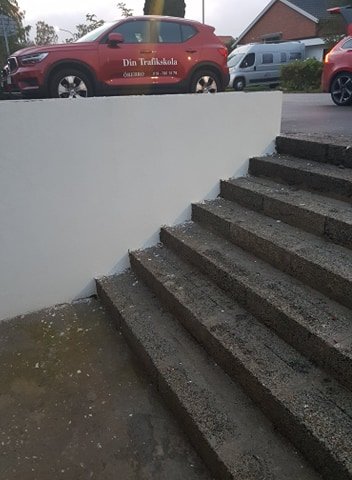 Nybyggd bred trappa av lecablock framför en vitputsad stenmur med parkerade bilar i bakgrunden.