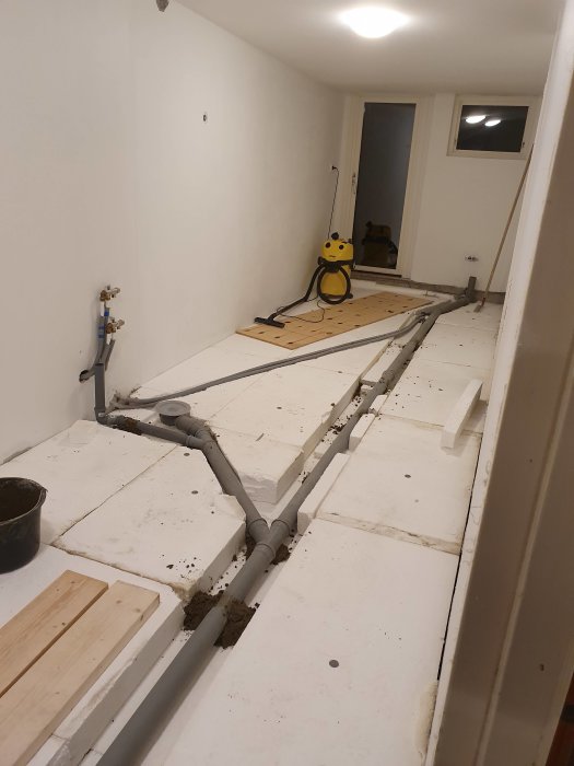 Avloppsrör som justerats i lutning längs ett golv under renovering inför betonggjutning.