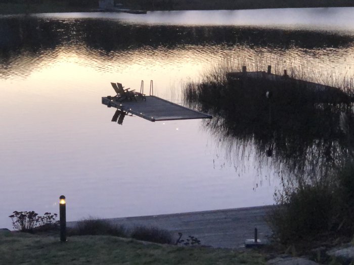 Översvämmad brygga vid sjö i skymning med ökad vattennivå och reflektioner.