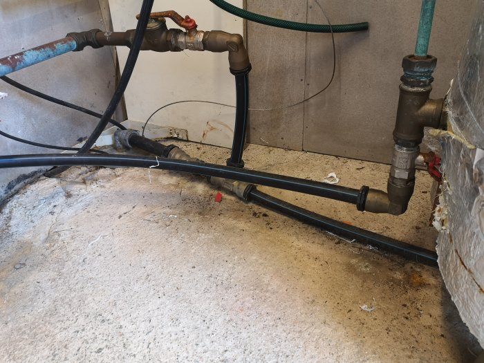 Vattenledningar och röranslutningar längs en smutsig betonggrund i ett pumprum.