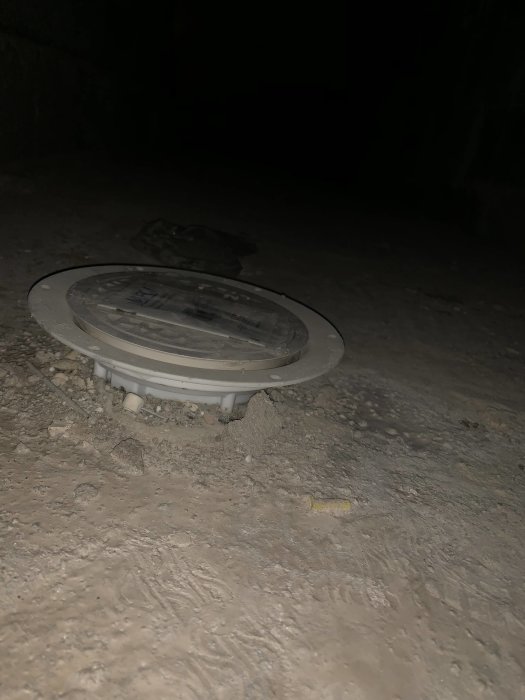 Plastbrunn i nygjuten betong med synlig grus och småsten på natten.