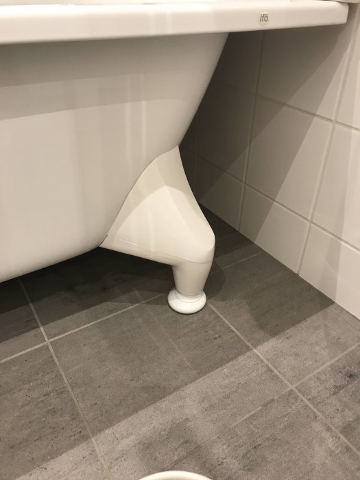 Vit plastfot till ett badrums handfat som ser oskadad och ren ut mot kakelvägg och klinkergolv.