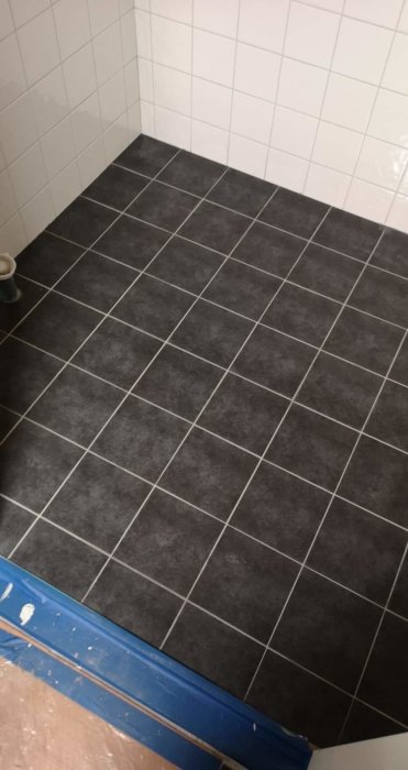Nyfogade mörkgrå klinkerplattor på badrumsgolv med vita kakelväggar.