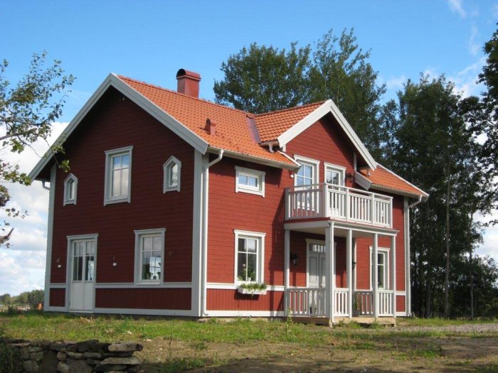 Rött trähus med vita knutar, sadeltak och en balkong som kan vara Eksjöhusmodellen Prästgården.