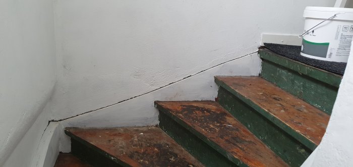 Trappa ner till källare med sliten grönmålad yta och stor springa mellan vägg och vangstycke.