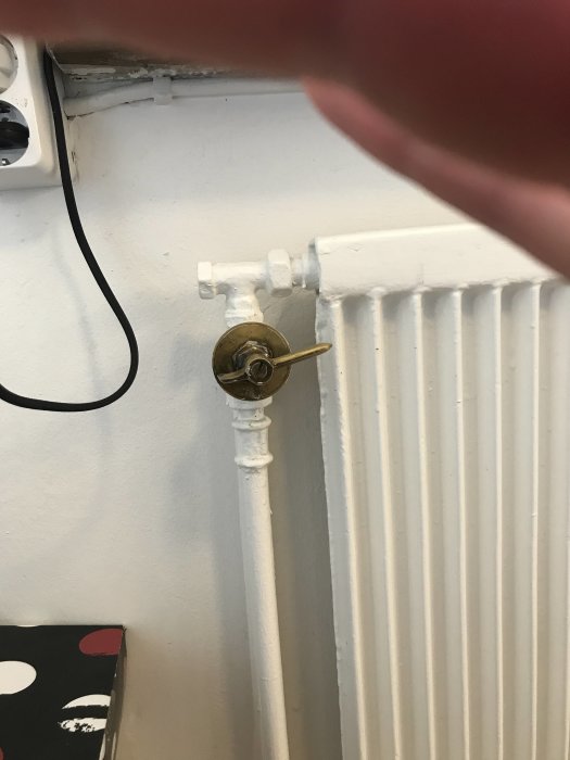 Rengjord och klarlackerad radiatorventil i mässing mot vitmålad radiator och vägg.