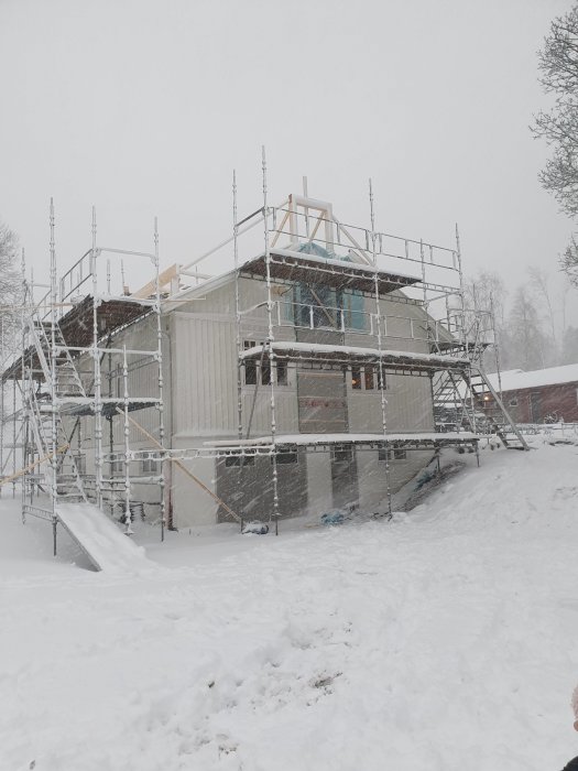 Hus under konstruktion täckt av snö med byggnadsställningar runt om.