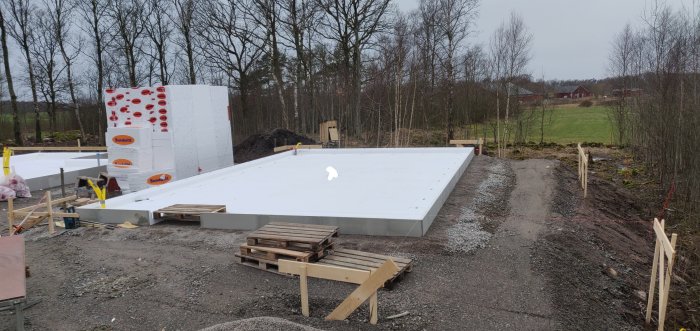 Grundarbete för garage med isolerade betongblock och träpallar, i ett landskap under uppbyggnad.