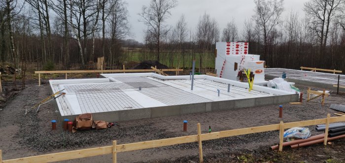 Grundarbete för garage med armeringsnät klart och byggmaterial i väntan på rörmokare.