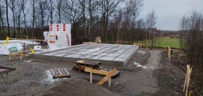 Grundarbeten för husbygge med synlig armering och isolerblock, pågående byggarbetsplats med grus och snörester.