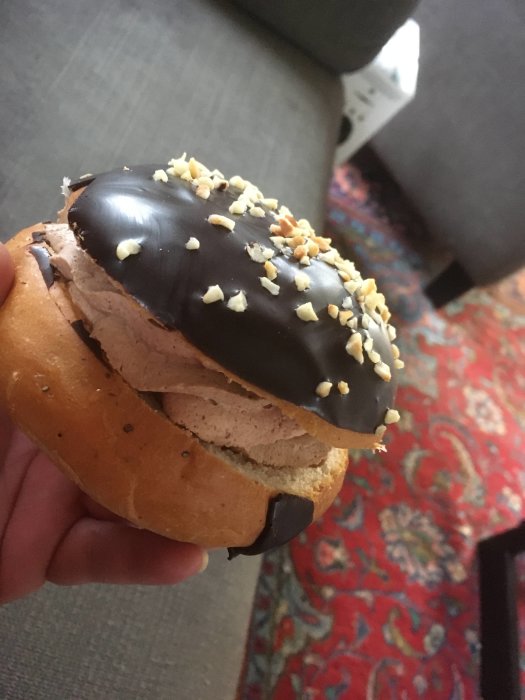 Svensk semla med chokladmousse, mörk chokladöverdrag och hackade hasselnötter, hålls i handen.