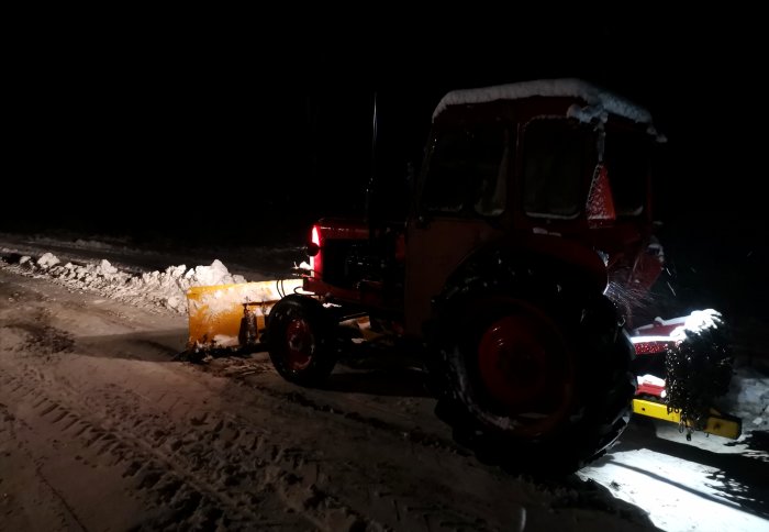 Röd Volvo BM T320 traktor med snöblad röjer snö på natten.