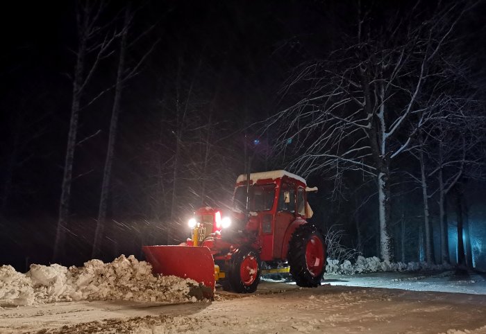 Röd Volvo BM T320 traktor med snöplog röjer snö nattetid.