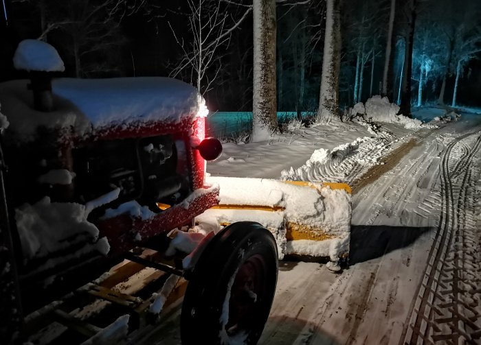 En snötäckt Volvo BM T320 traktor som använts för snöröjning på natten.