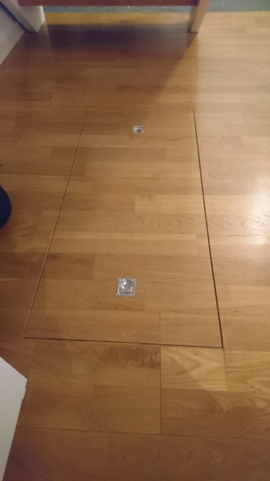 Trägolv med en lucka och två infällda metallringhandtag.